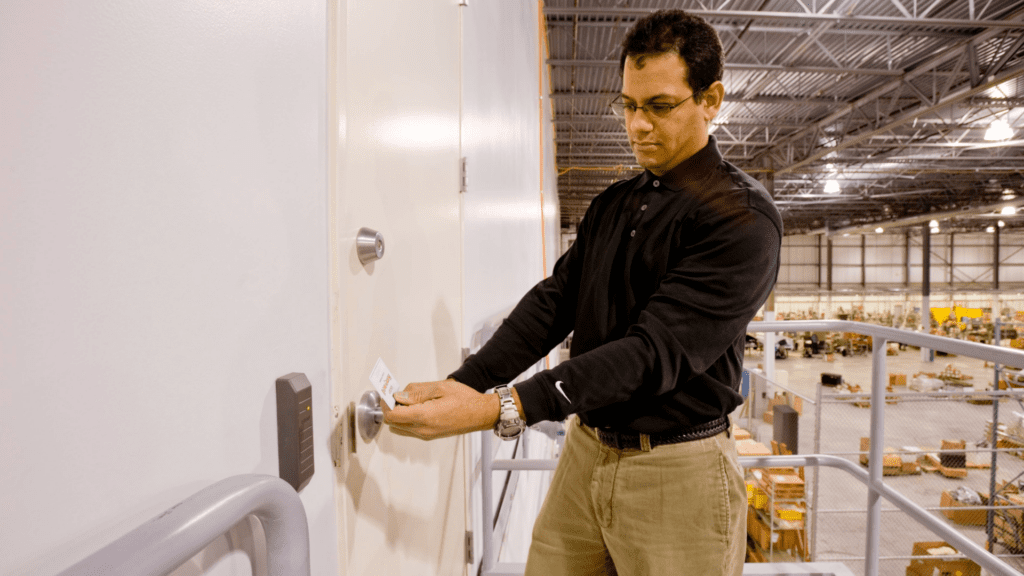 Man using the card reader and his employee card to scan into a door looking over a warehouse.