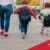 Woman holding hands with children wearing backpacks, walking down the street.