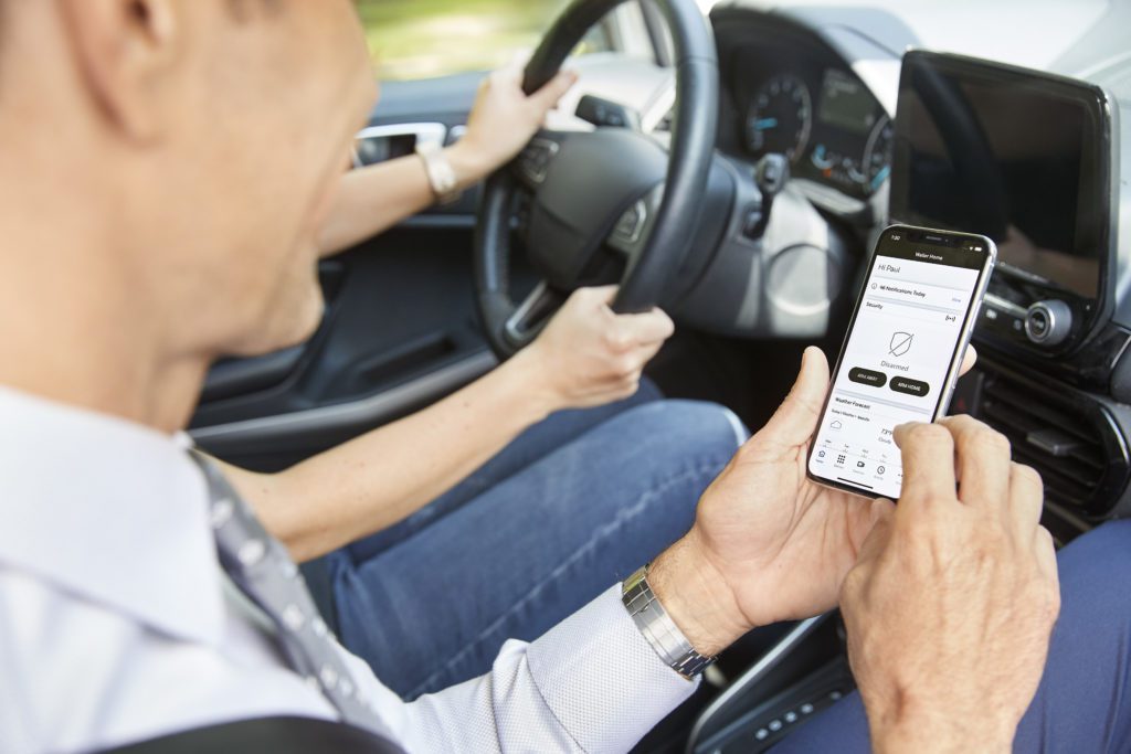 Person in the passenger seat of a vehicle interfaces with the Total Connect security app, on a smartphone. 