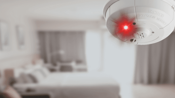 Carbon monoxide detector on ceiling blinking overtop a bedroom