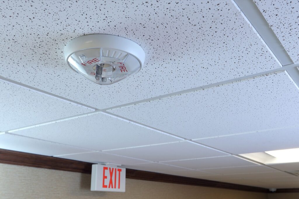 Fire alarm system. Strobe mounted on the ceiling with exit sign in the background.